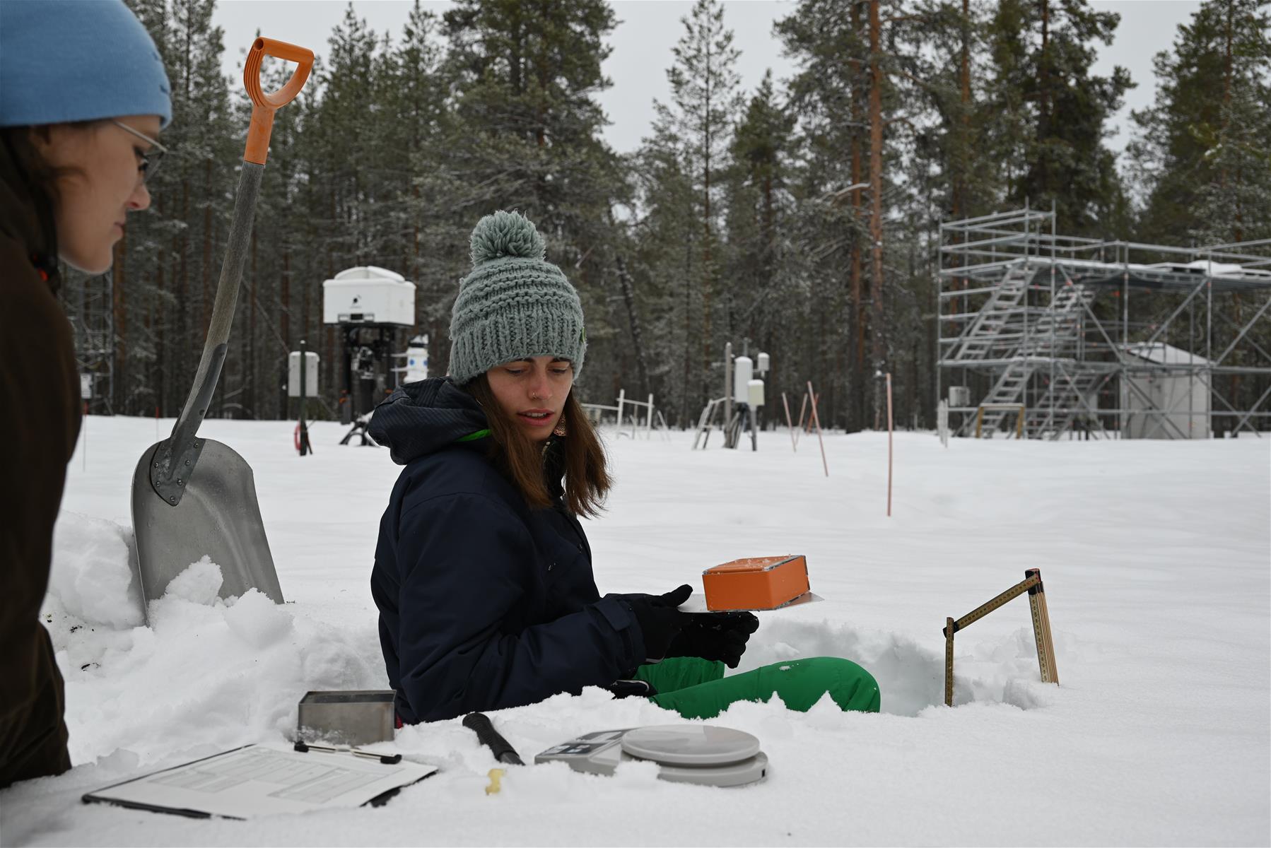 Leena Leppänen and Marina Falke sitting in the snow with measurement equipment.