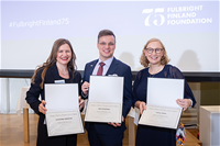 Kolme palkittua henkilöä hymyilevinä ryhmäkuvassa kunniakirjojen kera.