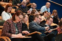 Hymyileviä seminaarin osallistujia luentosalissa kirjoittamassa muistiinpanoja.